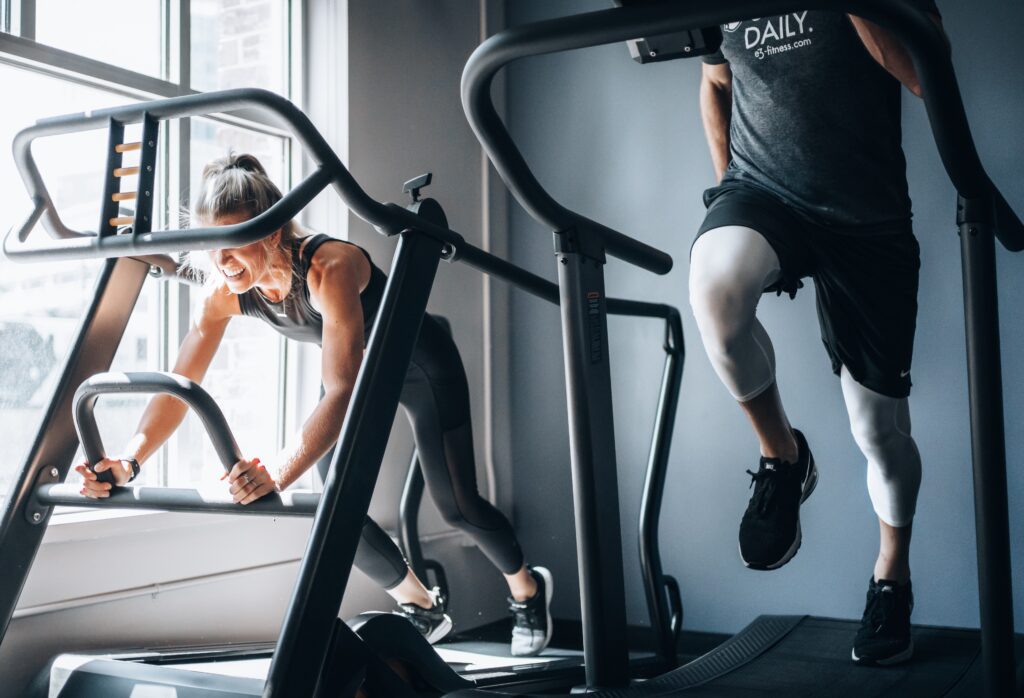 two people working out on exercise machines. One is running on a treadmill and you can only see the legs. The other is a woman doing core work. They're hitting their morning workout