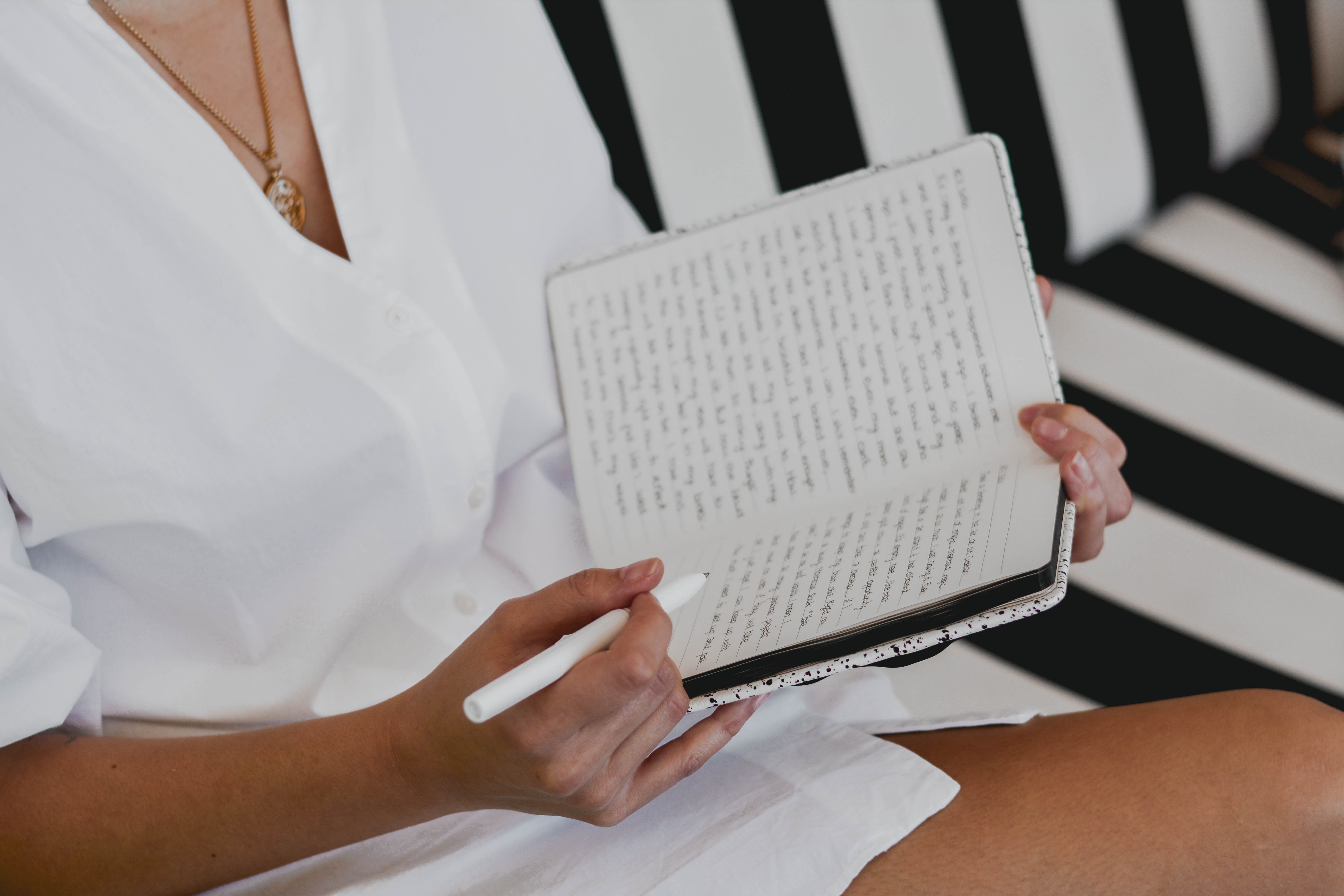 women writing using journal prompts in her journal. She's on a black and white couch.