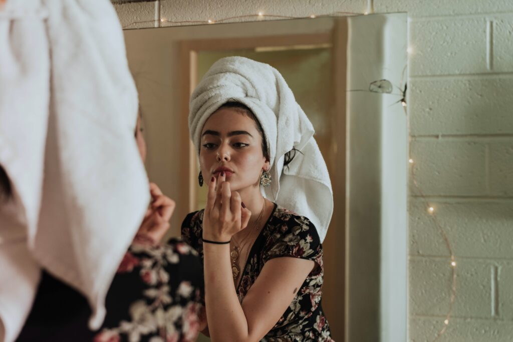 girl with towel on her head in the bathroom applying lip balm.
