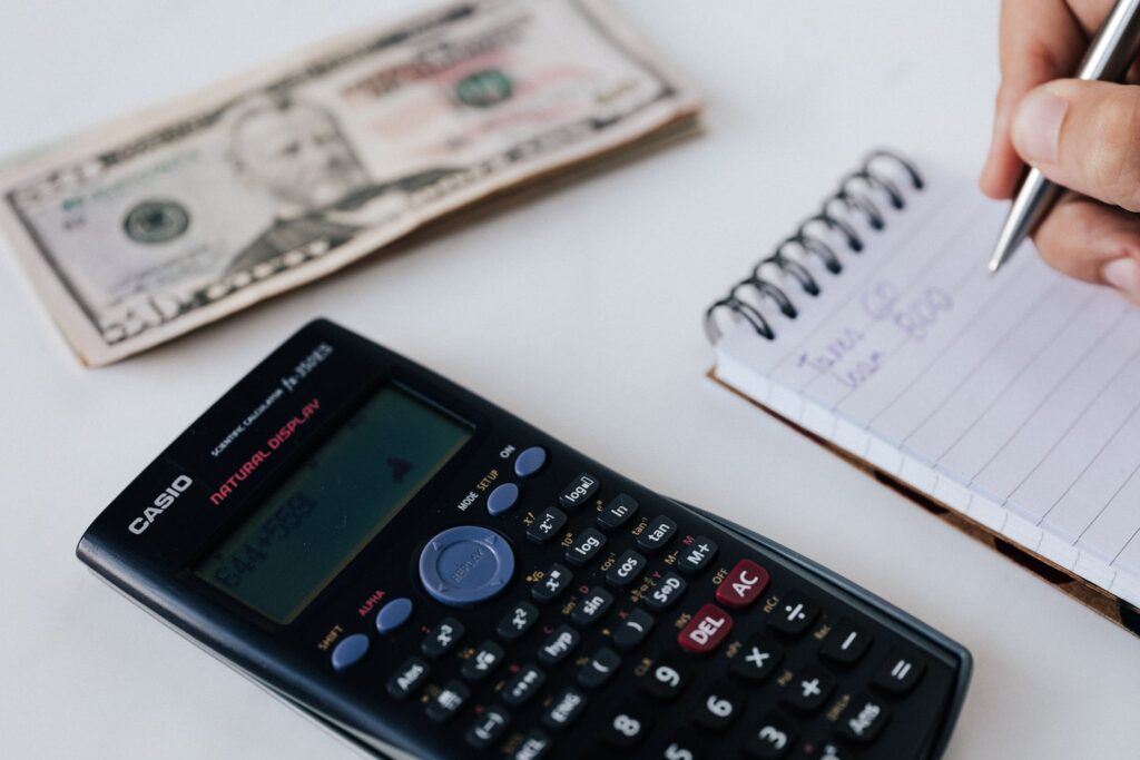 Crop unrecognizable accountant counting savings using notebook and calculator. Budgeting is a great way to accomplish your 2024 financial goals.