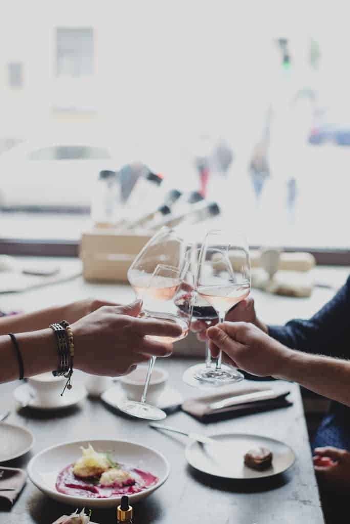 Anonymous friends clinking with wineglasses in restaurant during daytime while having fun and enjoying weekend together indoors in daytime during celebration. Brunch to maximize your weekends