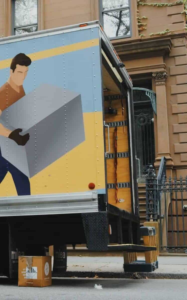 large moving truck with artwork of a man moving boxes on the side. The truck is open and men are loading more items into the back of the truck. moving to a new city.